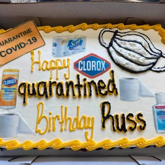 A birthday celebration idea where vanilla sheet cake is iced and decorated into a quarantine birthday cake. Icing has been used to draw on a mask and sanitizers, clorox and toilet paper has been digitally printed on. The border is yellow and the cake says Happy Quarantined Birthday Russ